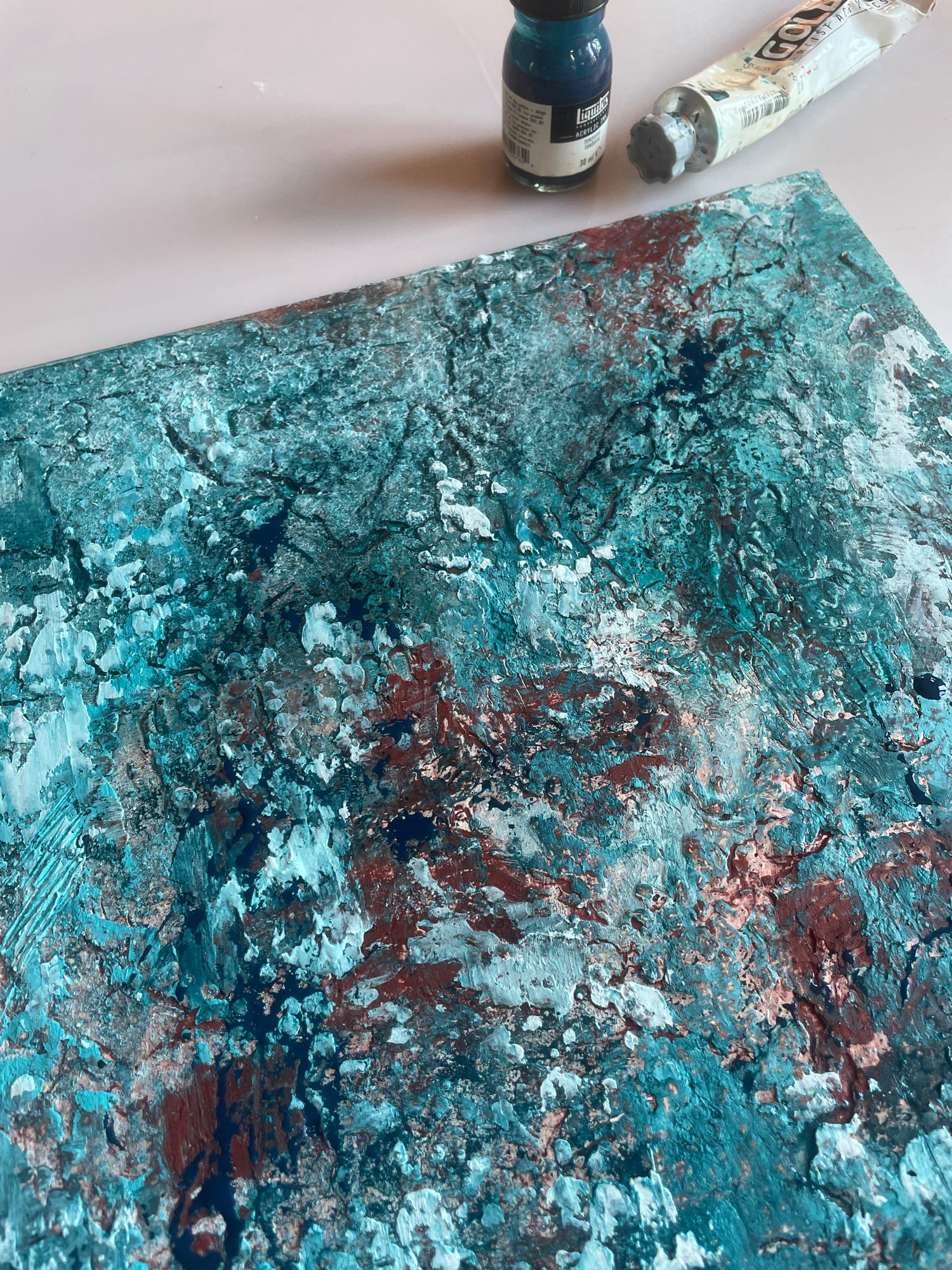 Couches acryliques turquoise, blanches et rougeâtres avec des reliefs, à côté de peinture et d’encre sur la table de Marina