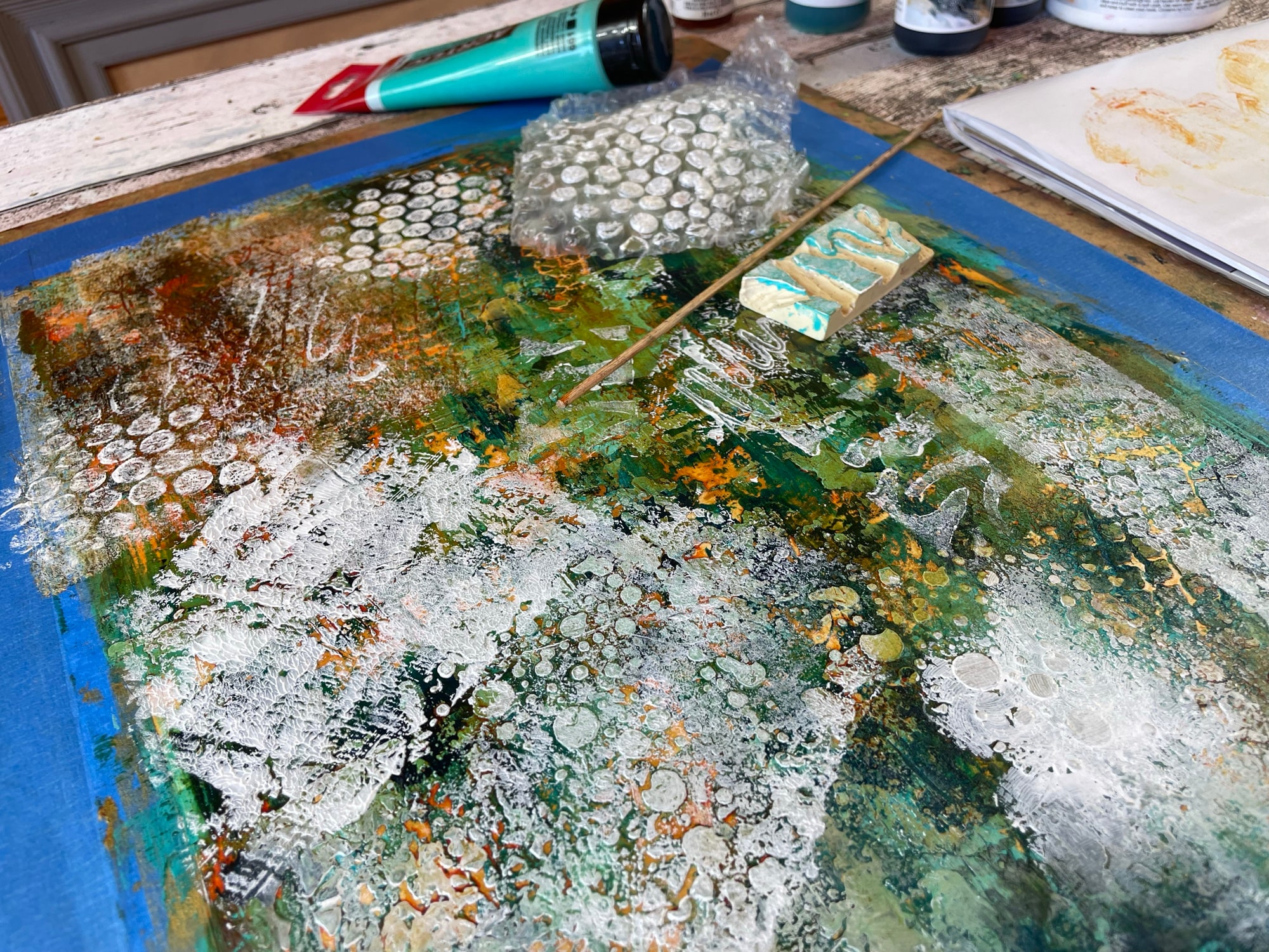 Du papier bulle et un tampon fait main déposent de la peinture blanche sur des couches acryliques colorées