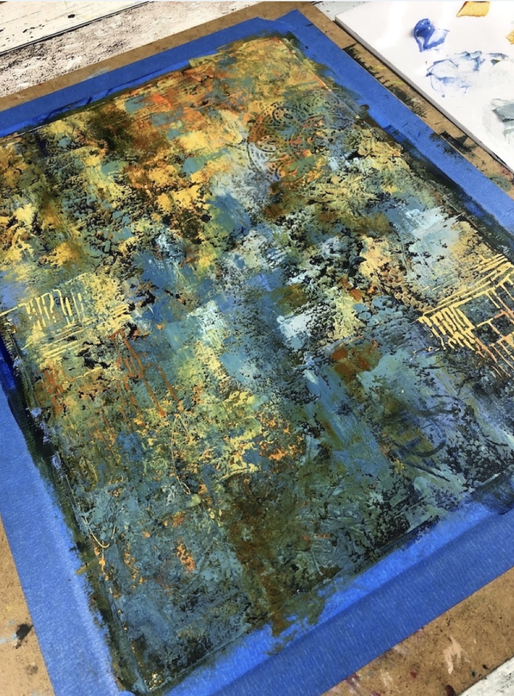 Un fond abstrait bleu et doré fixé à une planche avec du ruban, avant que Marina ajoute la figure