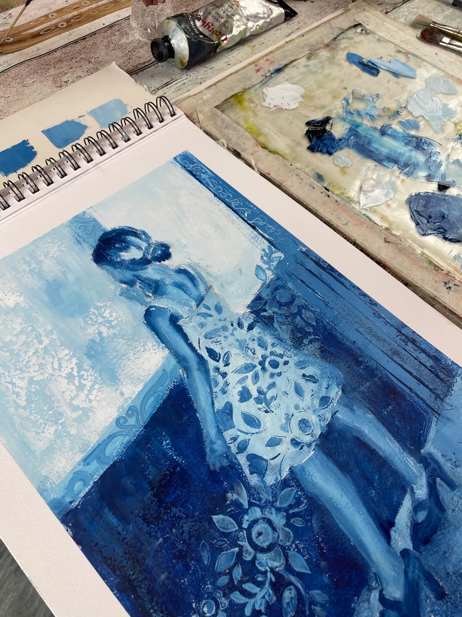 Peinture libre d’une petite fille en bleu dans le carnet de Marina, à côté d’une palette de bleus clairs et foncés