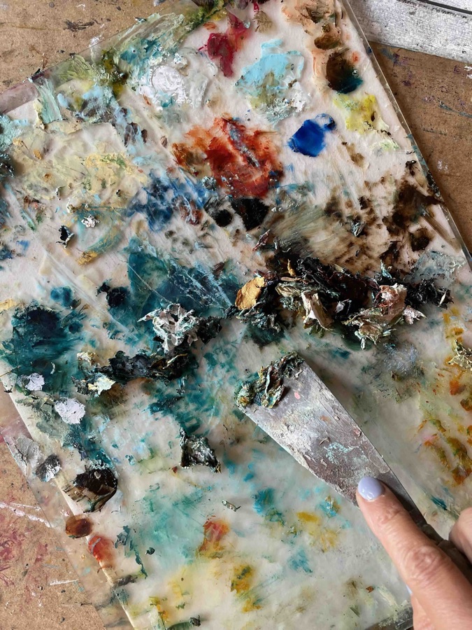 Marina's glass palette covered in scraped paint, with a palette knife in her hand
